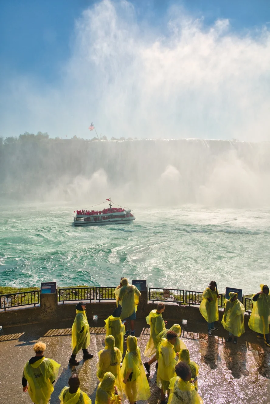 Guided tour group boarding Niagara City Cruises boat with American Falls and Bridal Veil Falls visible