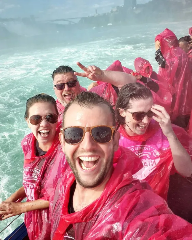 Smiling tourists in ponchos taking a selfie on a Niagara Falls boat tour